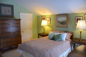 Ein Schlafzimmer mit Bett, Kommode, Nachttischen und Wandbildern.