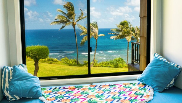 A room with a large window overlooking a beach with palm trees and the ocean.