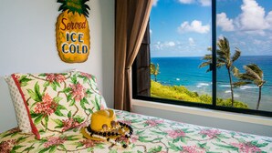 A bed with a floral bedspread, a pineapple-shaped sign, and a view of the ocean through a window.