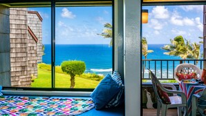 A room with a large window overlooking the ocean, a bed with a colorful quilt, and a table with a striped tablecloth.