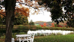 Une table de pique-nique et des bancs au bord d’un lac, avec le feuillage automnal en arrière-plan.