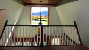 Une vue depuis un balcon doté d’une balustrade en bois, d’un luminaire suspendu et d’une fenêtre donnant sur un paysage composé d’arbres et de montagnes.
