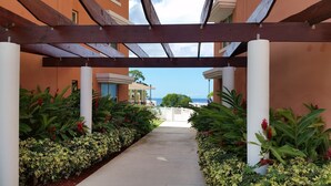 A covered walkway with a view of the ocean, flanked by lush greenery and a building with a white facade. - Beautiful Mediterranean Style Ocean View Villa, Spectacular Sunsets!  (Aguadilla)