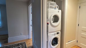 A laundry room with stacked washers and dryers, a patterned rug, and wooden flooring.