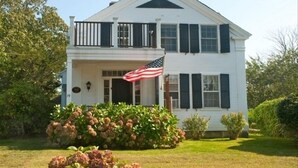 A two-story white house with black shutters, a balcony, and an American flag.