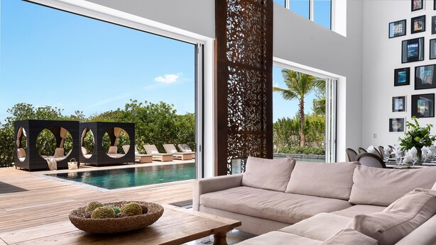 A modern living room with a large beige sofa, a wooden coffee table with decorative balls, and a view of a pool and outdoor seating area.