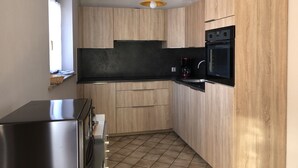 Eine kleine Küche mit Holdekor-Schränken, einer schwarzen Arbeitsplatte, einem eingebauten Backofen und einer hängenden Pendelleuchte.