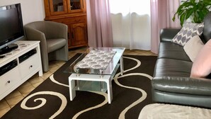 Ein Wohnzimmer mit Fernseher, Sofa, Couchtisch, Schrank und Vorhängen.