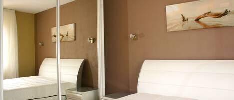 A bedroom with a bed, a nightstand, a mirror, and a painting on the wall.