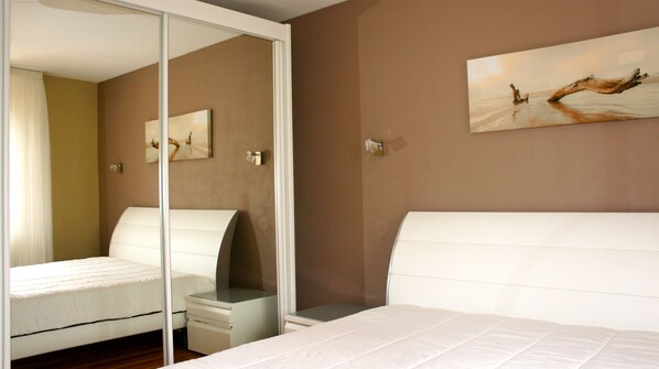 A bedroom with a bed, a nightstand, a mirror, and a painting on the wall.