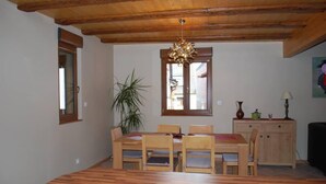Een eetruimte met een houten tafel en stoelen, een kroonluchter, een potplant en een kast met decoratieve objecten.