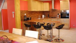 Een keuken met houten kastjes, een centraal eiland met barkrukken, een roestvrijstalen afzuigkap en een oven.