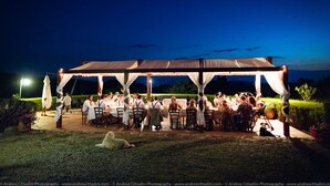 An outdoor gathering under a tented area with tables and chairs arranged for dining.