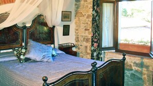 A bedroom with a four-poster bed, stone walls, and a window with a view of greenery.