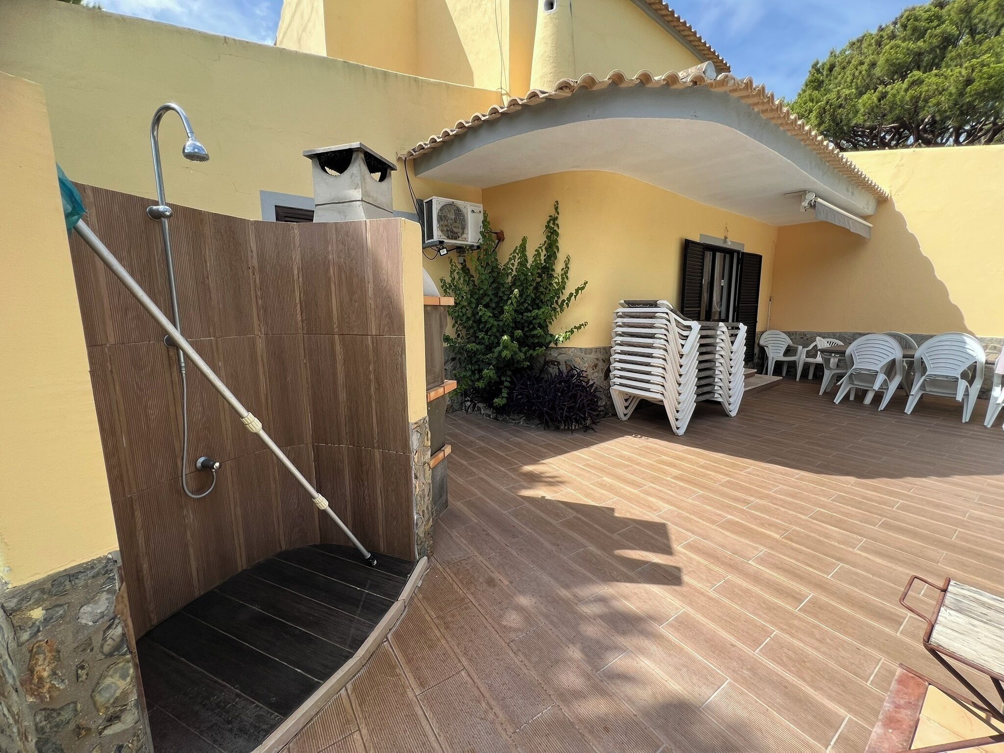 Un patio con una scala in legno, sedie da esterno e pavimento piastrellato.