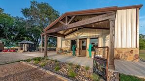 A rustic building with a 'Welcome' sign, a covered patio, and a sign for 'Desert Hills Hotel'. - Custom Barndominium Perfect For Romantic Getaways, Lake or Family Vacations (Caldwell)
