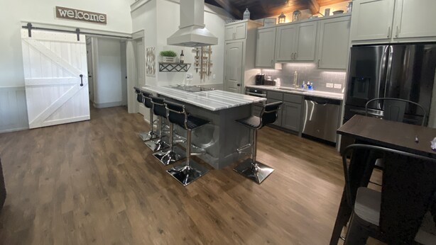 A modern kitchen with a central island, bar stools, and a stainless steel refrigerator. - Custom Barndominium Perfect For Romantic Getaways, Lake or Family Vacations (Caldwell)