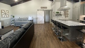 A spacious living area with a high ceiling, a checkered sofa, a dining bar with stools, and a kitchen area with a large island. - Custom Barndominium Perfect For Romantic Getaways, Lake or Family Vacations (Caldwell)