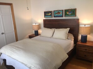 A neatly made bed with two bedside tables, each with a lamp, and three framed artworks above the bed.