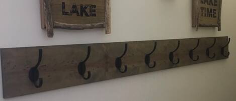 Dos letreros de madera en una pared, uno dice "WELCOME TO THE LAKE" y el otro "ON LAKE TIME". Abajo, hay un perchero metálico con ganchos.