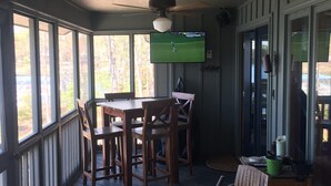 En inglasad veranda med ett bord och stolar, en takfläkt och en tv som visar en golfmatch.