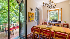 Un comedor con una mesa grande, sillas y un candelabro. También hay un escritorio con una silla y una planta.