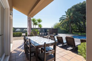 Une terrasse extérieure avec une table et des chaises, une piscine et des palmiers.
