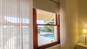 A room with a window overlooking a swimming pool, a radiator below the window, and a bedside table with a lamp. - Luxury villa with pool close to the beach (Póvoa de Varzim)