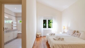 A bedroom with two beds, a window with curtains, a bedside table with a lamp, and a bathroom with a tiled floor and a sink. - Luxury villa with pool close to the beach (Póvoa de Varzim)