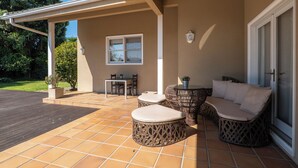 A covered patio with a wooden deck, wicker furniture, a table with chairs, and a window. - Luxury villa with pool close to the beach (Póvoa de Varzim)