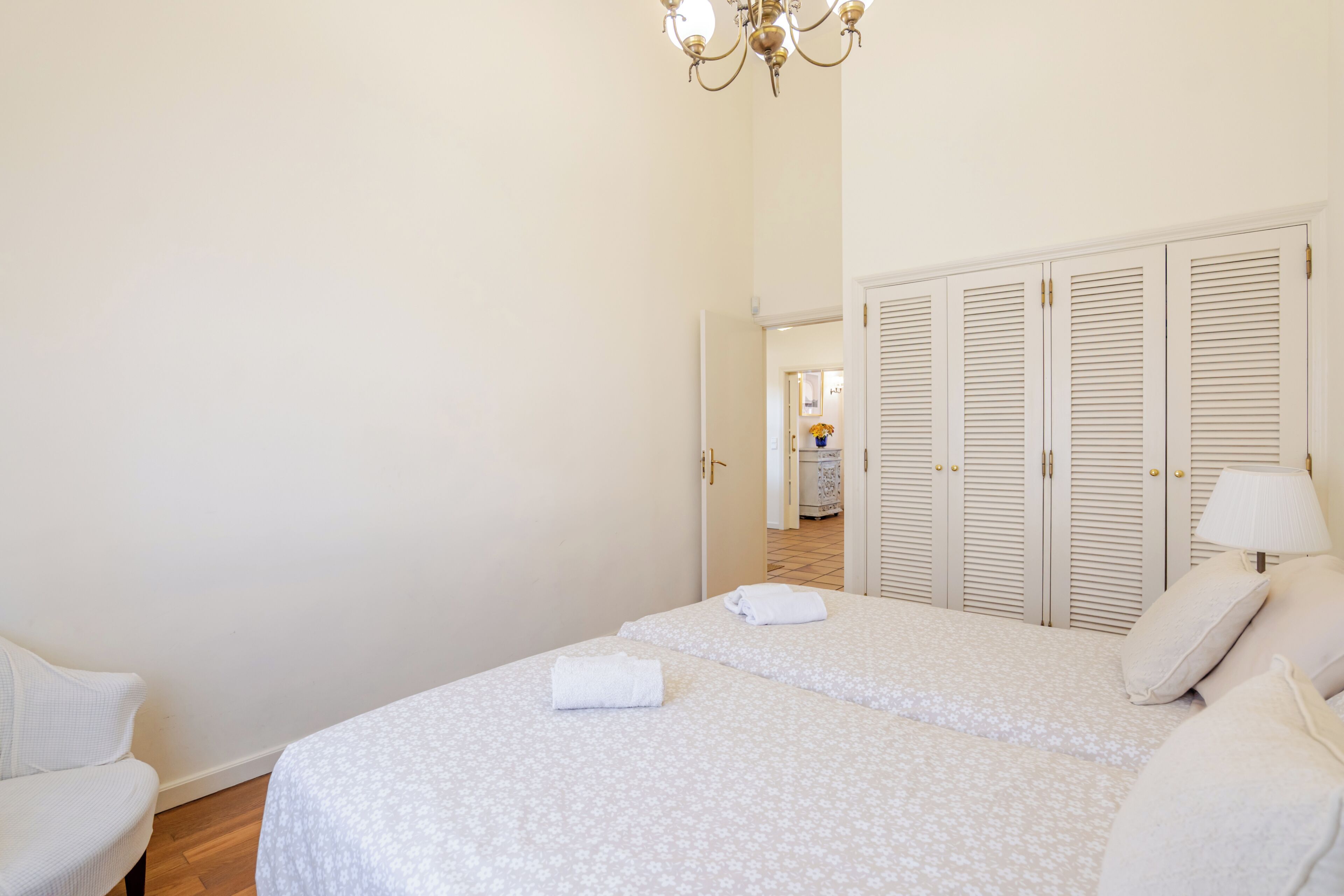 Une chambre avec deux lits, un lustre, une armoire et une porte donnant sur une salle de bain.