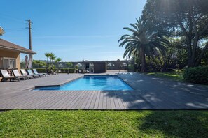 Une piscine avec une terrasse en bois, des chaises longues et une maison en arrière-plan.