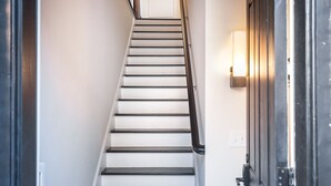 A staircase with white steps and black handrails, leading to a door with a light fixture on the wall beside it. - Modern Farmhouse Style, 1 Block from Forsyth Park by Lucky Savannah (Savannah)