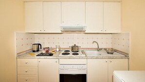 Una cocina con gabinetes blancos, una estufa, un lavamanos y una tetera.