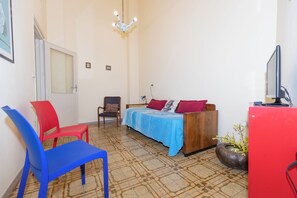 Quarto com cama, cadeira, escrivaninha, televisão e um vaso de planta.