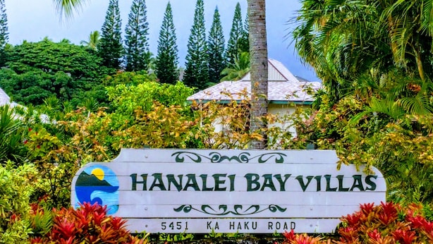 A sign for Hanalai Bay Villas with a scenic view of lush greenery and a building in the background. -  Villa  in Paradise !Mountain Views, Ocean and golf course just  steps away (Princeville)