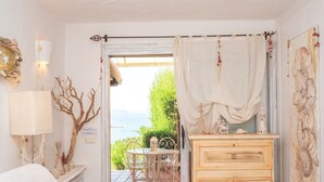 Una habitación con vista al mar, un aparador de madera, una mesa con sillas y una lámpara.