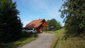 Een huis met een rood dak, een verharde oprit en een auto ervoor geparkeerd.
