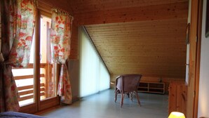 Een slaapkamer met een schuine kap, een bed, een stoel en een lamp.
