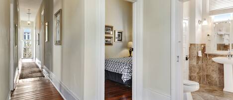A hallway with wooden flooring, a bed with patterned bedding, and a bathroom with a sink and toilet.