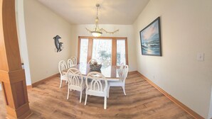A dining area with a table and chairs, a chandelier, a wall-mounted painting, and a window with blinds. - Beautiful Secluded Canalfront Home. Access to Private Beaches and Marina (Kitty Hawk)