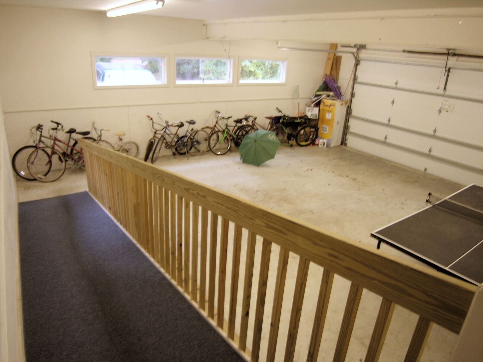 Een garage met fietsen, een tafeltennistafel en een groene paraplu.