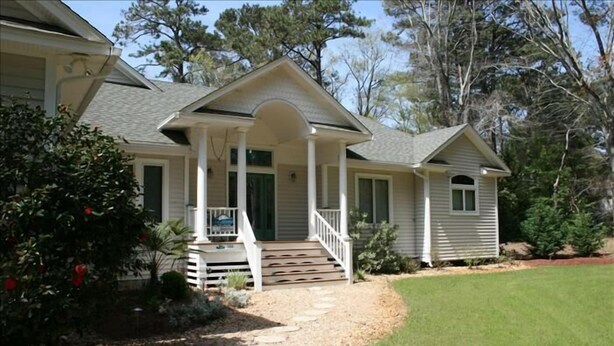 A two-story house with a front porch, a covered entryway, and a small front yard with a gravel path. - Beautiful Secluded Canalfront Home. Access to Private Beaches and Marina (Kitty Hawk)