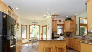 A spacious kitchen with wooden cabinets, a black refrigerator, a central island with stools, and a ceiling fan. - Beautiful Secluded Canalfront Home. Access to Private Beaches and Marina (Kitty Hawk)
