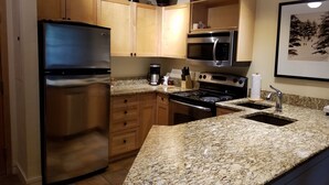 Une cuisine moderne dotée d’appareils électroménagers en acier inoxydable, de plans de travail en granit, d’armoires en bois et d’un luminaire suspendu.