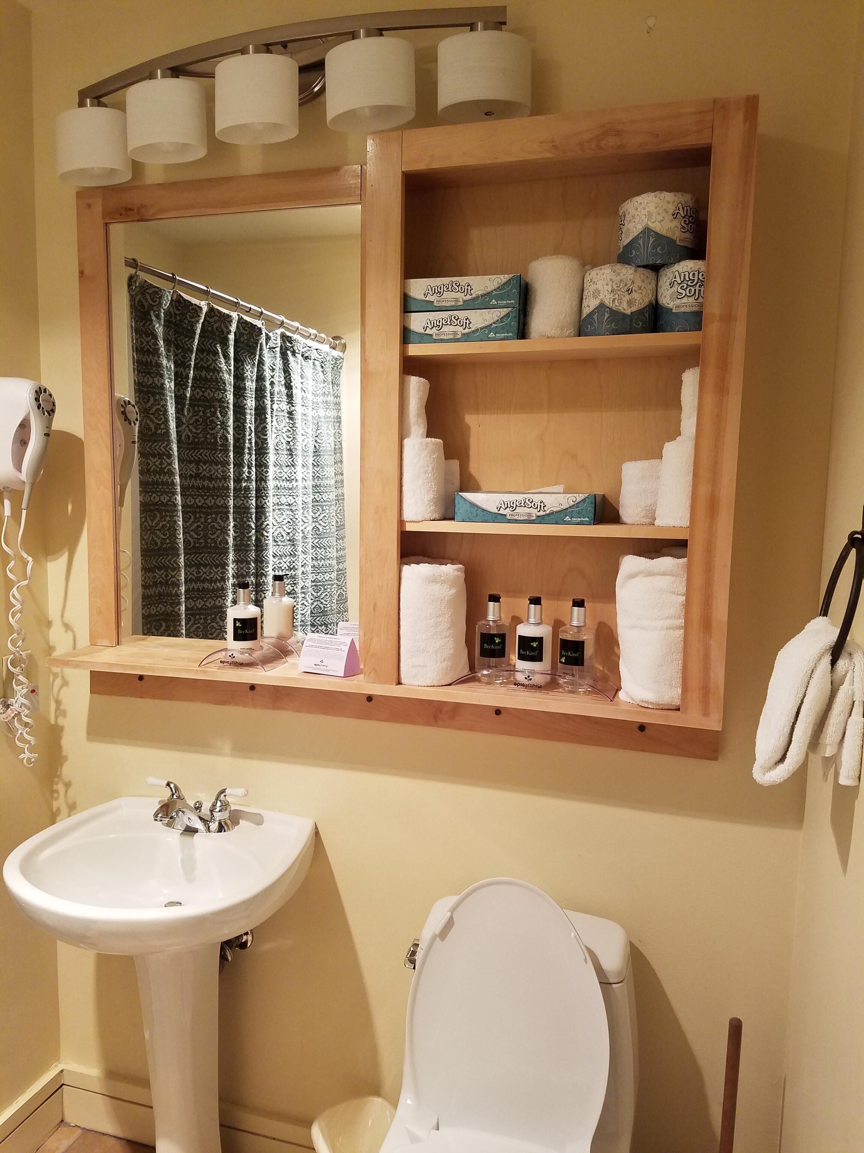 A bathroom with a white sink, toilet, and a shelf with toiletries.