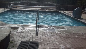 Une piscine avec un escalier en métal, entourée d’un chemin piétonnier en briques.