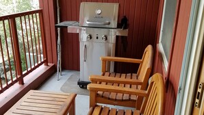 Un balcon équipé d’un barbecue de type Char-Broil, de chaises en bois et d’une table.