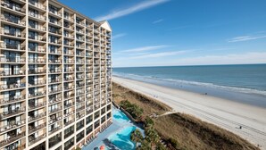 Un hotel de gran altura con múltiples balcones, vistas a la playa y una zona de piscina.