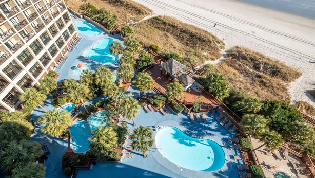 Vista aérea de un resort con varias piscinas, palmeras y una playa.